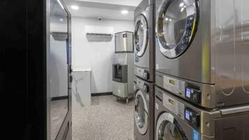 Un cuarto de lavandería con lavadoras y secadoras apiladas, un dispensador de agua y un refrigerador pequeño.