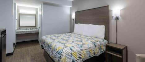 Une chambre d’hôtel avec un lit, une table de chevet et un petit bureau avec une chaise.