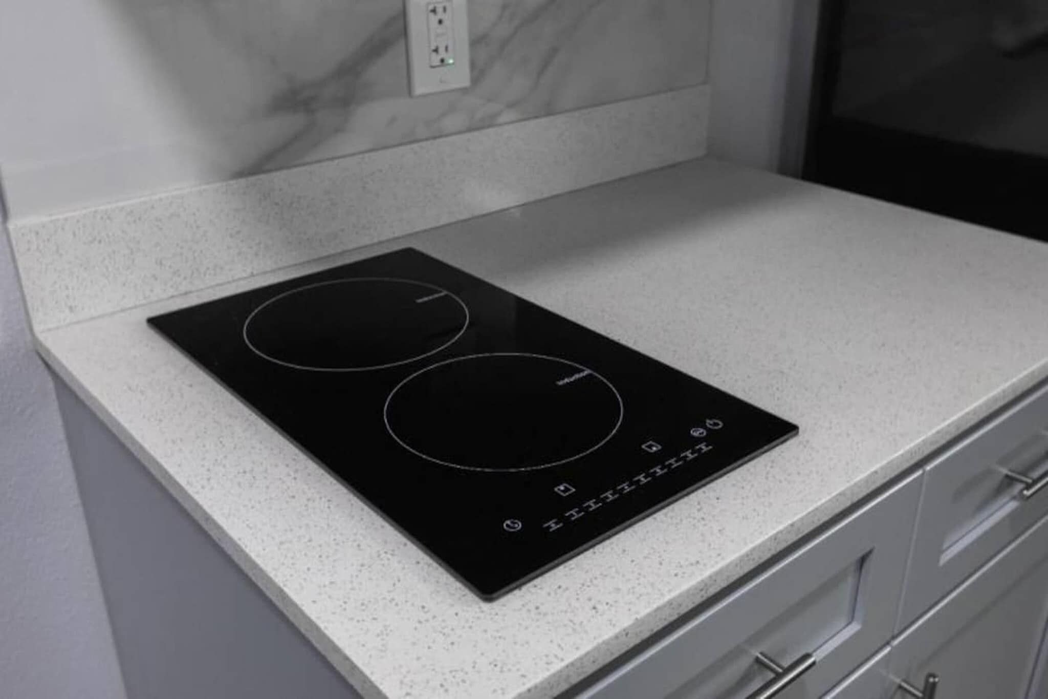 Una cocina de inducción negra sobre una encimera blanca con un salpicadero de mármol.