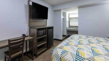 A hotel room with a bed, a desk with a chair, a television, and a small kitchenette.