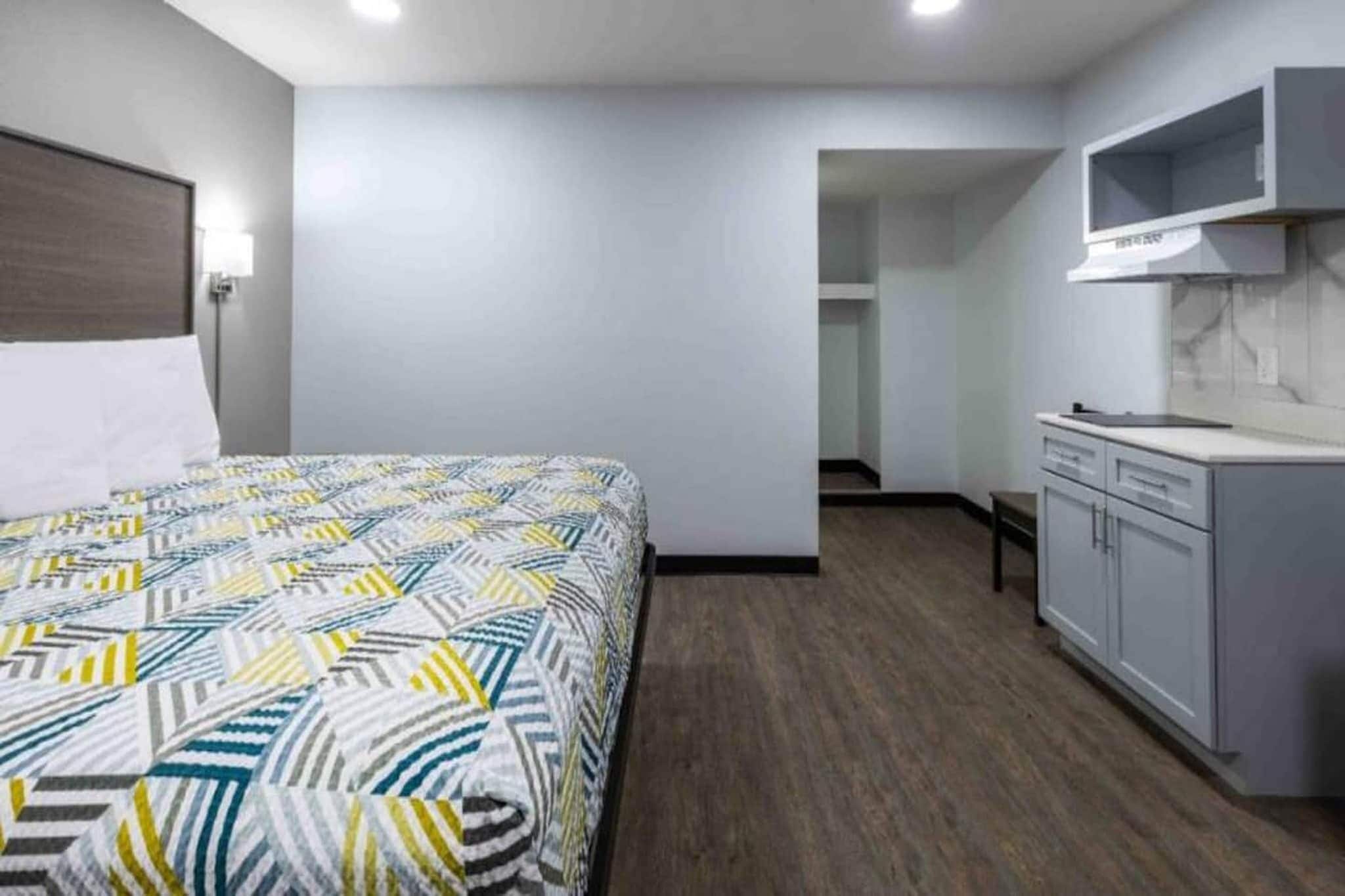 A hotel room with a bed, a kitchenette, and a bathroom visible through an open door.