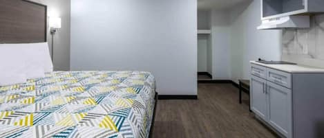 A hotel room with a bed, a kitchenette, and a bathroom visible through an open door.