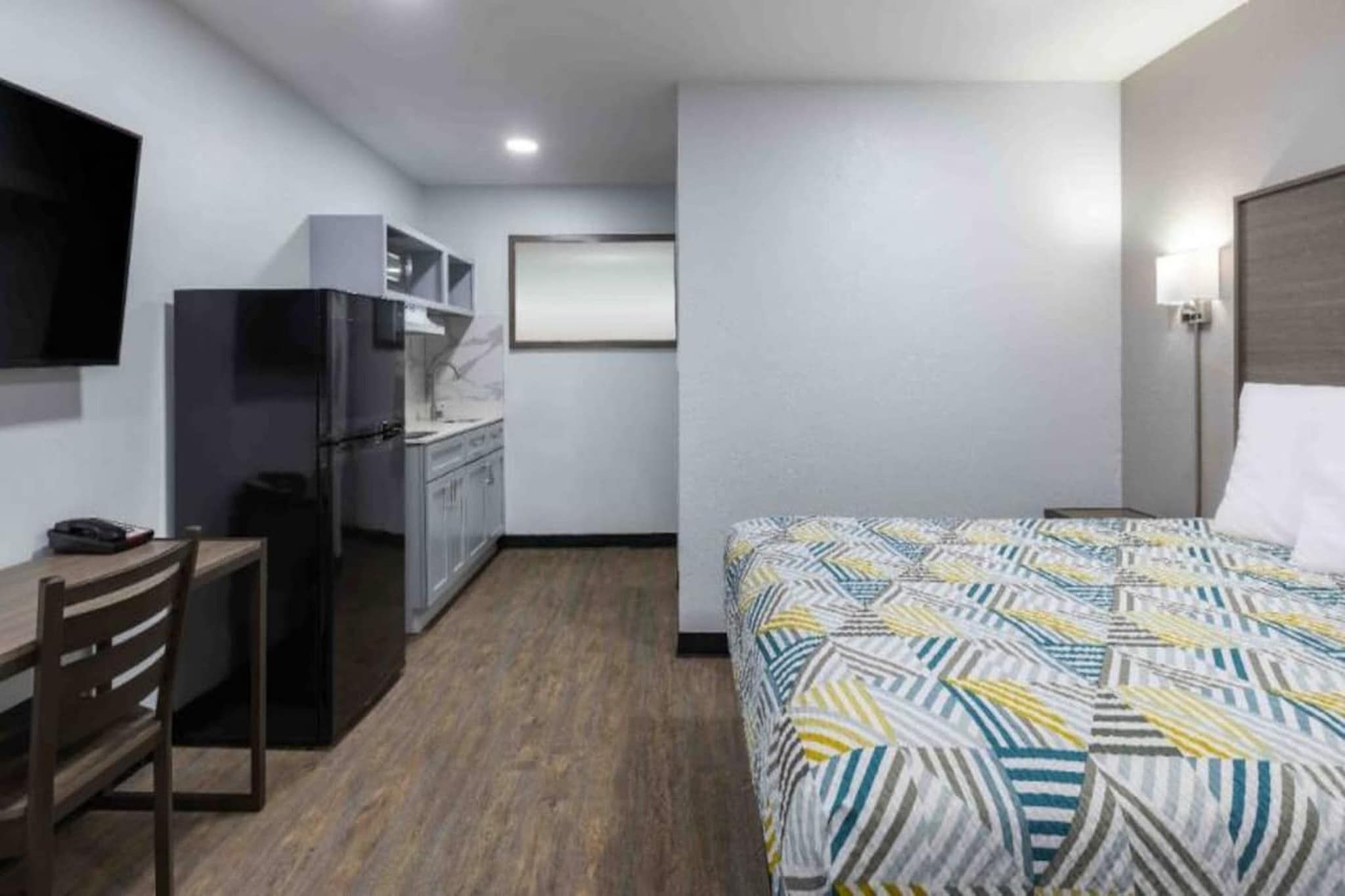 Habitación de hotel con cama, escritorio, silla, kitchenette y televisor.