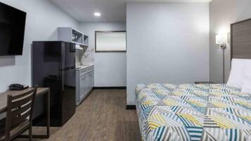 Habitación de hotel con cama, escritorio, silla, kitchenette y televisor.