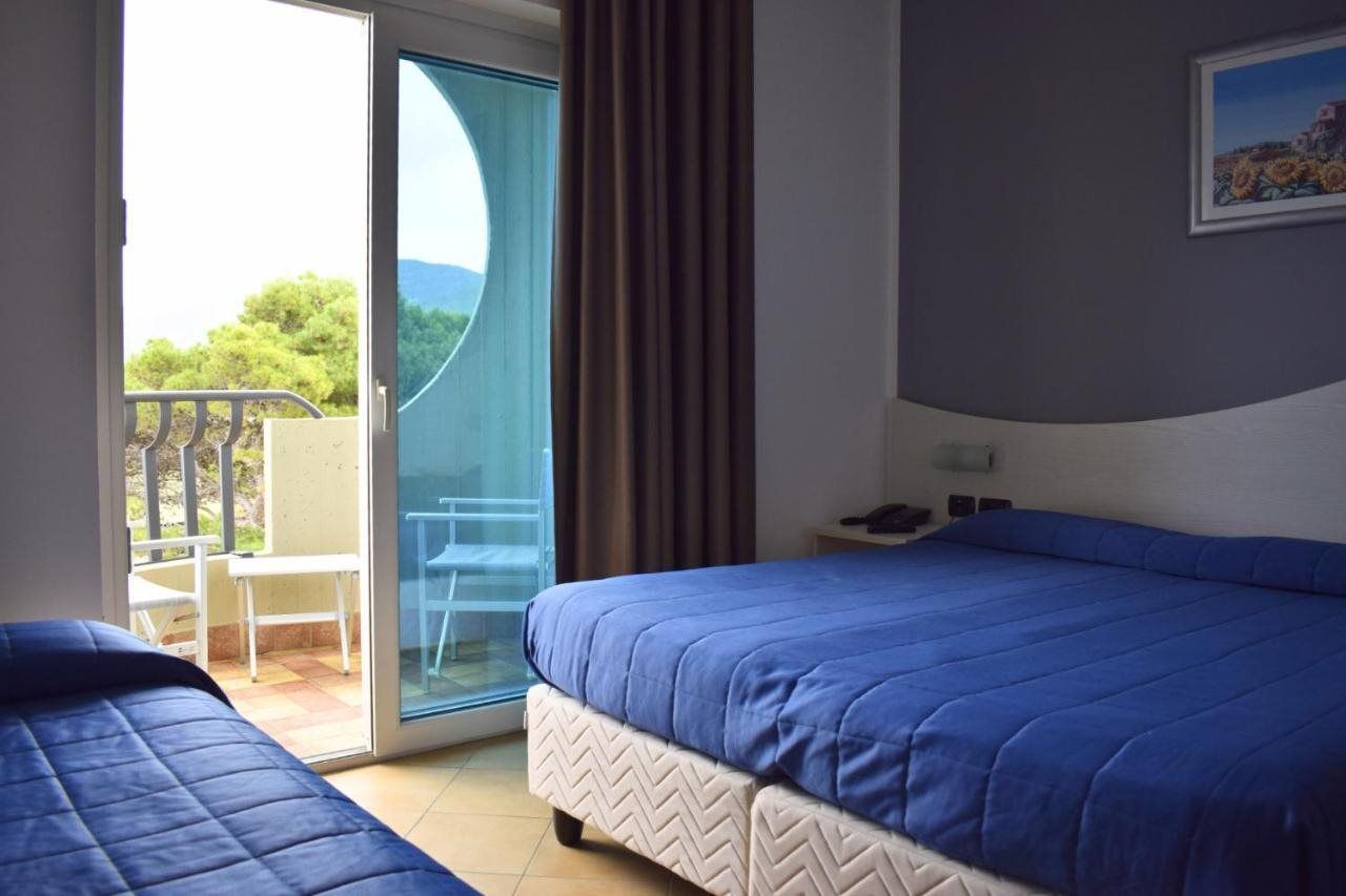 A hotel room with a bed, a chair, a table, and a view of the outdoors.