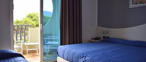 A hotel room with a bed, a chair, a table, and a view of the outdoors.
