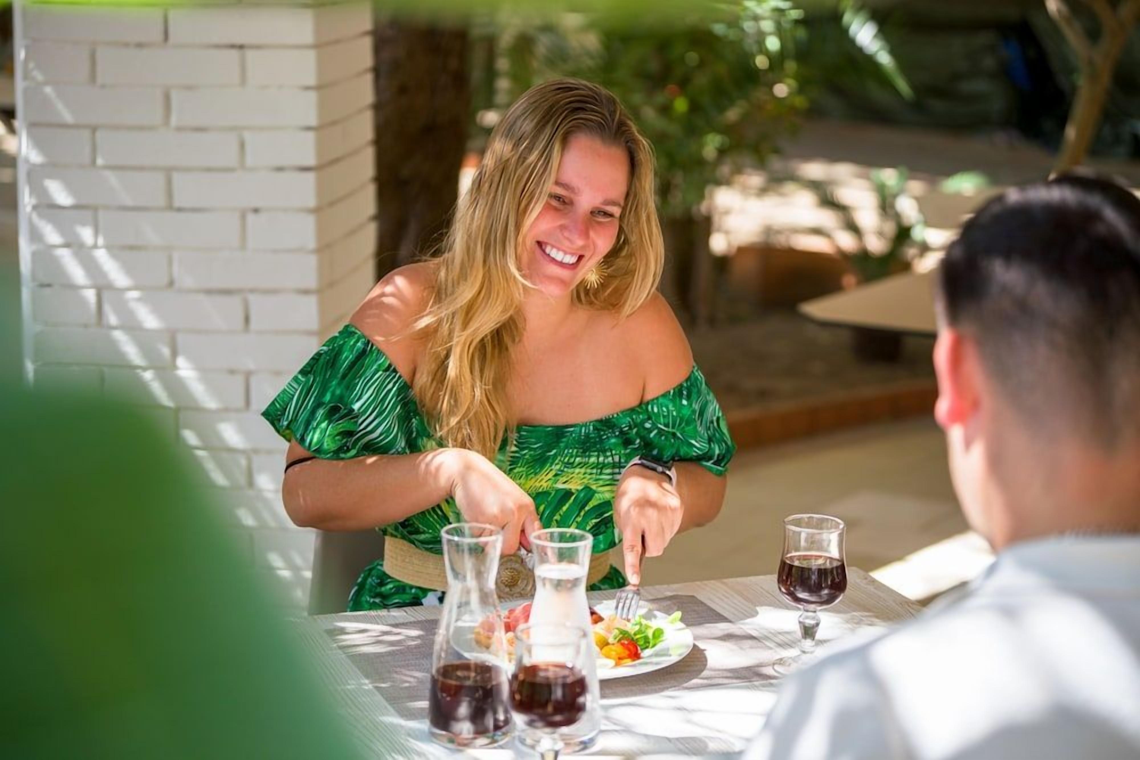 A dining table with a meal, two glasses of red wine, and a bottle of water.