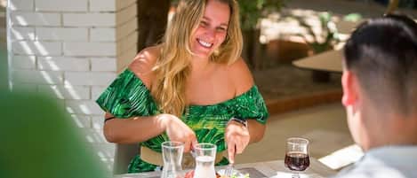 A dining table with a meal, two glasses of red wine, and a bottle of water.