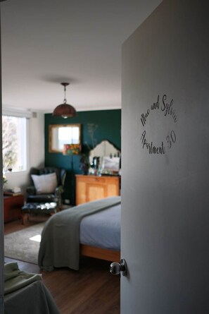 Un dormitorio con cama, cómoda y ventana. Hay una puerta con un letrero que dice 'Mac and Sylvia Apartment 30'.