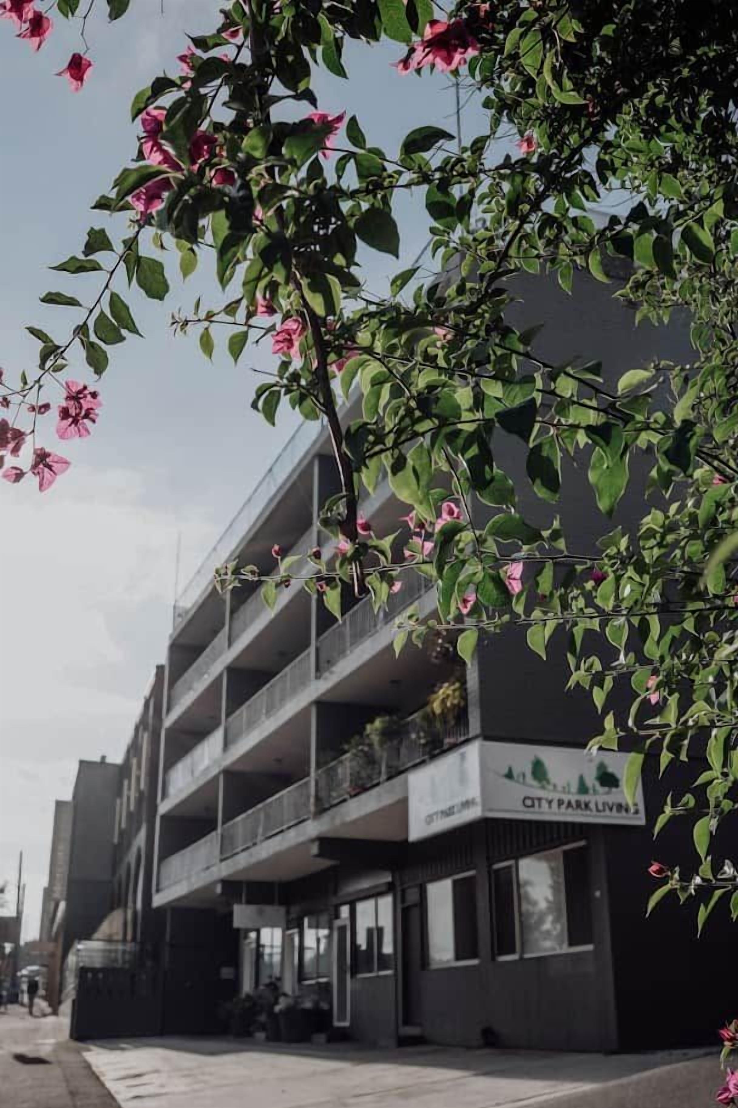 A multi-story building with balconies, a sign reading 'CITY PARK LIVING,' and a clear sky.