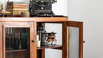 Armário de madeira com portas abertas, exibindo utensílios de cozinha e uma máquina de escrever antiga em cima.
