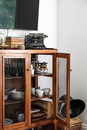 Un mueble de madera con puertas abiertas que muestra utensilios de cocina y una máquina de escribir antigua en la parte superior.