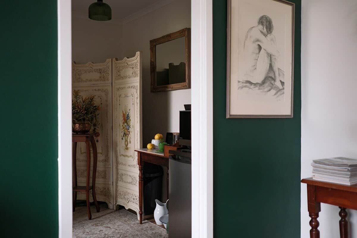 Quarto com escrivaninha, cadeira, espelho e uma obra de arte emoldurada na parede.
