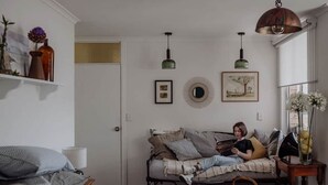 Een gezellige slaapkamer met een bed, een bank en een zithoek, met een persoon. Er zijn decoraties aan de muur en een hanglamp.