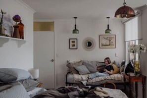 A cozy bedroom with a bed, a sofa, and a reading area with a person. There are wall decorations and a hanging light fixture. - Mac & Sylvia Luxe Spa Bath City Escape (Launceston)