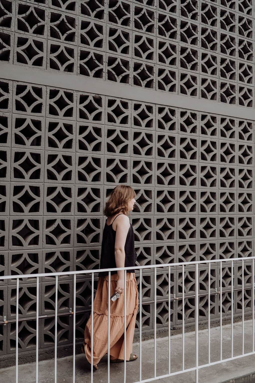 A person standing in front of a patterned wall with a metal fence in the foreground.