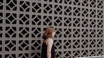 A person standing in front of a patterned wall with a metal fence in the foreground.