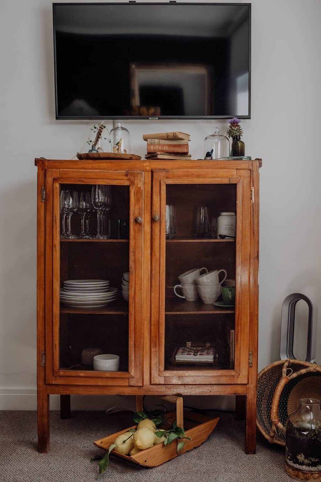 Een houten kast met glazen deuren, gevuld met keukengerei en boeken.