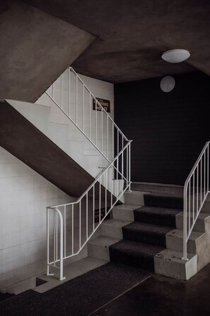 Una escalera con barandillas blancas y peldaños oscuros, que conduce a una habitación oscura con una lámpara en el techo.