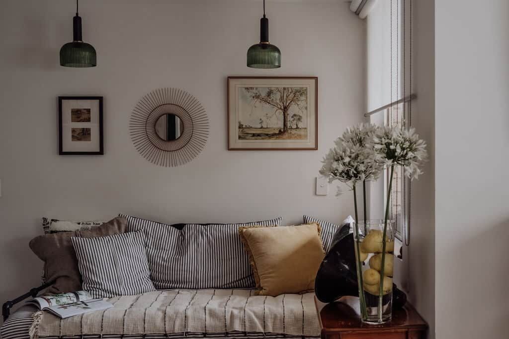Um quarto com um sofá listrado, um espelho redondo e um quadro na parede.