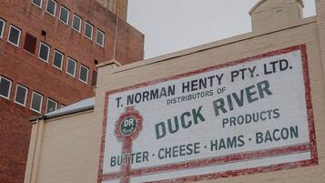 A building with a sign for T. Norman Henty Pty. Ltd., distributors of Duck River products like butter, cheese, hams, and bacon.