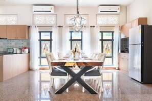 A modern kitchen with a dining area, featuring a wooden table, white chairs, and a black X-shaped base. - Naka Pool Villa Pratumnak Pattaya (Pattaya City)