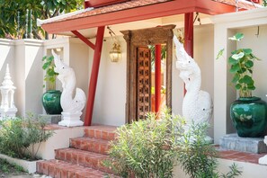 A building entrance with a red roof, a wooden door, and white statues. - Naka Pool Villa Pratumnak Pattaya (Pattaya City)