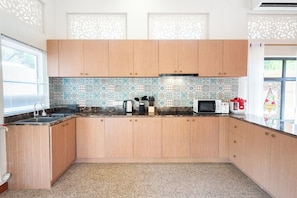 A kitchen with wooden cabinets, a tiled backsplash, a microwave, a coffee maker, and a window with blinds. - Naka Pool Villa Pratumnak Pattaya (Pattaya City)