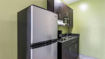 A compact kitchen with a stainless steel refrigerator, a microwave, and dark wooden cabinets.