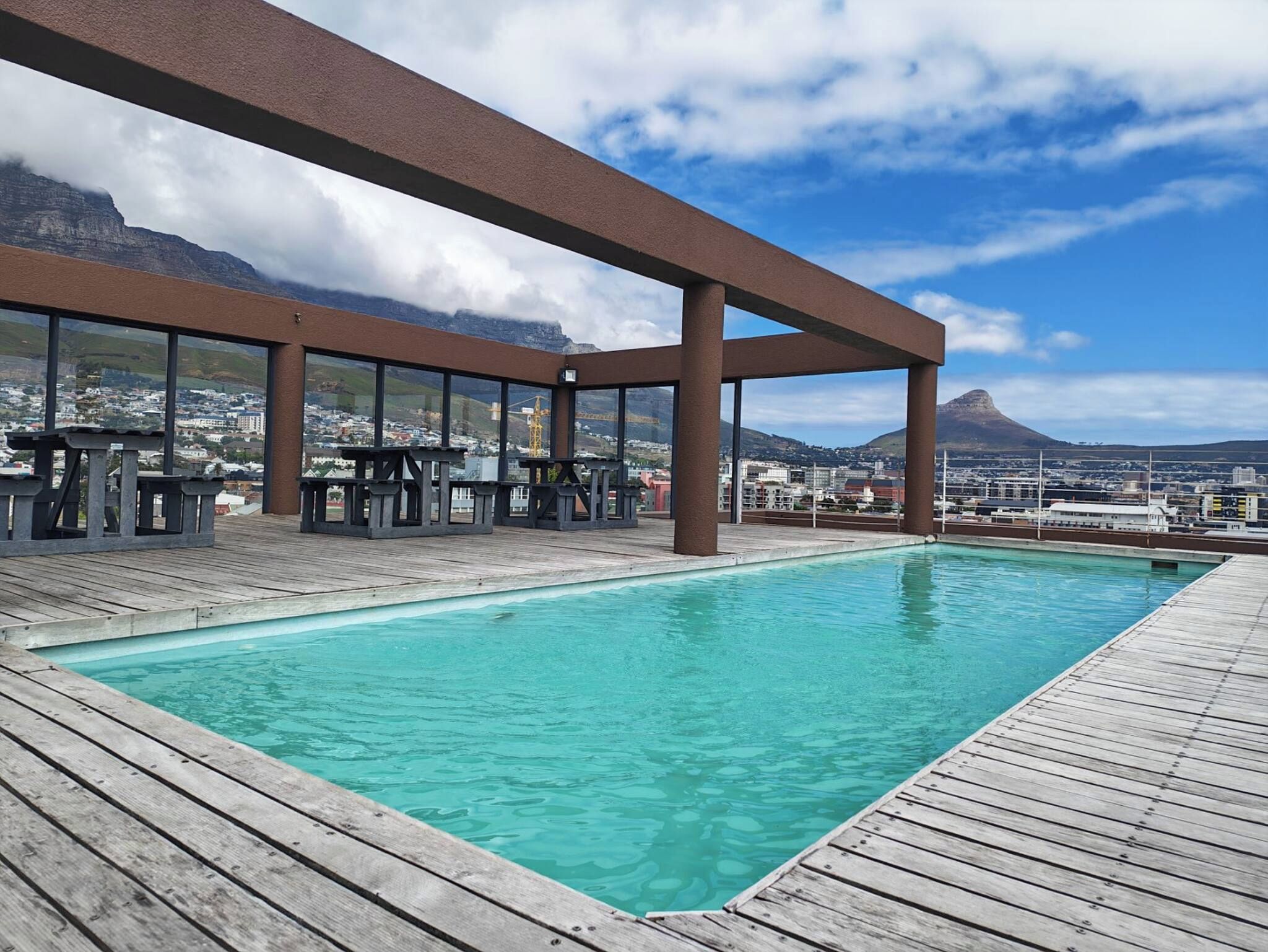 A swimming pool with a wooden deck and a view of a cityscape and mountains.