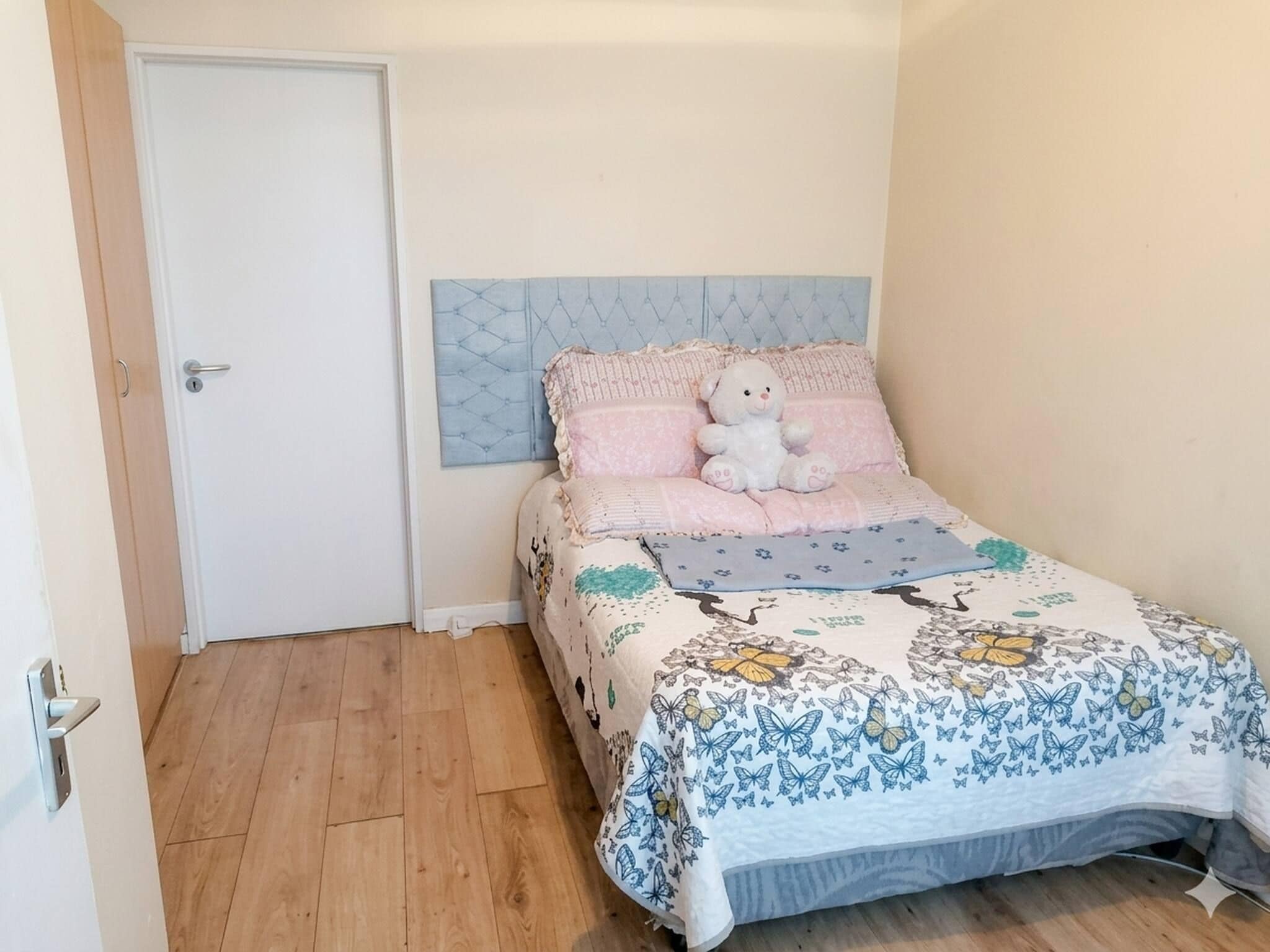 A bedroom with a bed, a white door, and a wooden floor.