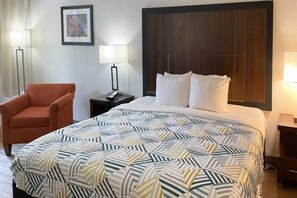 A hotel room with a bed, a chair, a nightstand, and a wall-mounted picture. - 1 King Bed | Non-Smoking (Opelika AL)