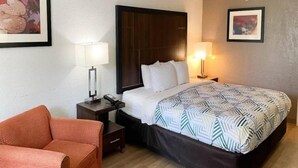 Hotellihuone, jossa on sänky, kaksi yöpöytää, tuoli ja pieni sivupöytä.
