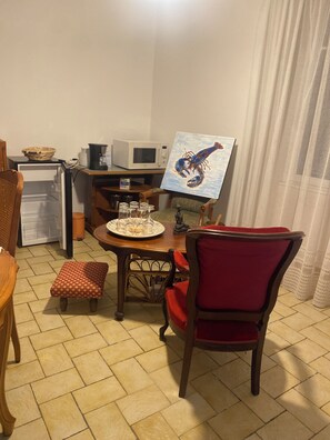 A dining area with a table set for two, a microwave, a refrigerator, and a painting on the wall. - Vrbo Property (Bains-sur-Oust)