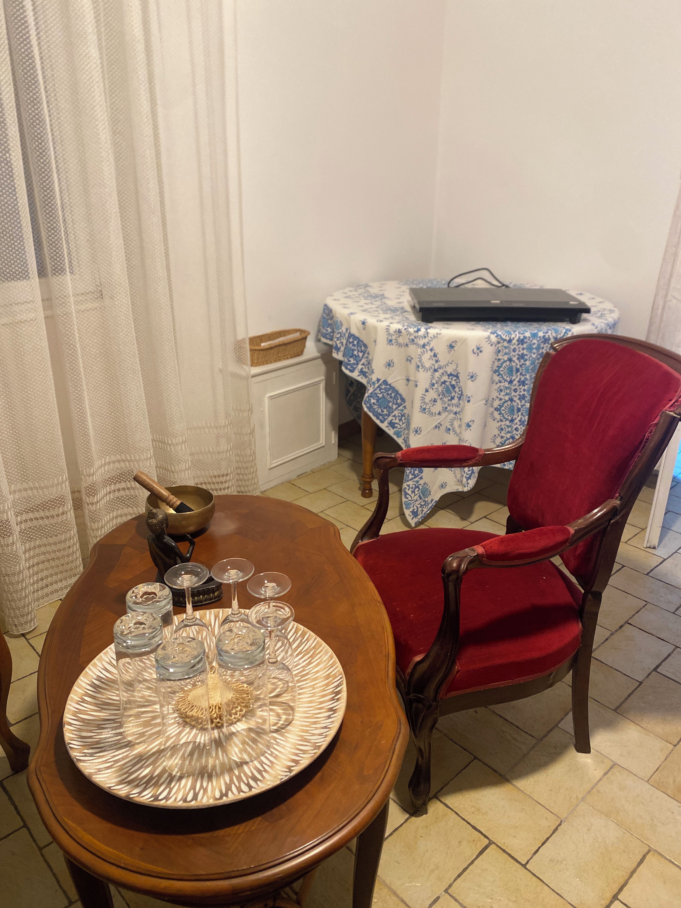 A dining area with a wooden table set for four, a red upholstered chair, and a small round table with a blue and white tablecloth.