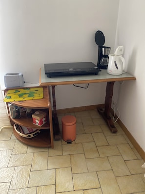 Une petite cuisine équipée d’un grille-pain, d’une machine à café et d’un ordinateur portable, le tout posé sur une table en bois.