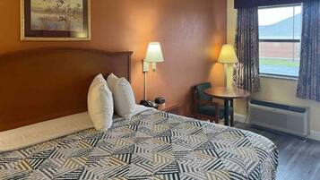 Une chambre d’hôtel avec un grand lit, deux lampes de chevet, une petite table, une chaise et une fenêtre avec des rideaux.
