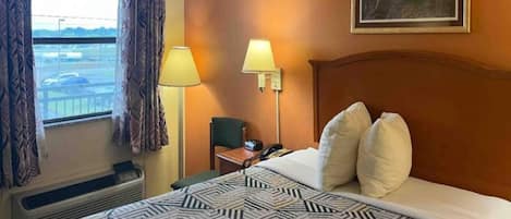 Ein Hotelzimmer mit einem großen Bett, zwei Nachttischlampen, einem Sessel, einem Schreibtisch mit Telefon und einem Vorhangfenster.