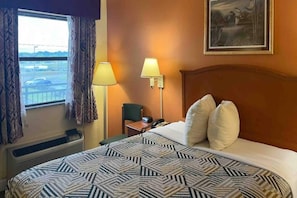 Une chambre d’hôtel avec un grand lit, deux lampes de chevet, une chaise, un bureau avec un téléphone et une fenêtre avec des rideaux.