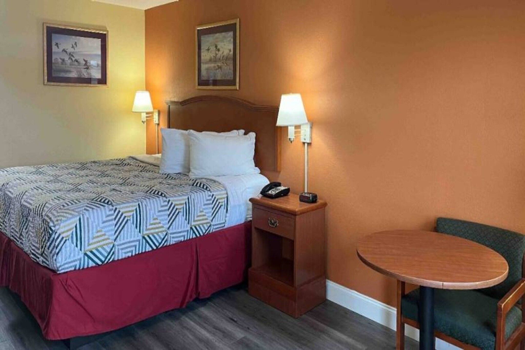 A hotel room with a bed, bedside lamps, a nightstand, and a small round table with a chair.