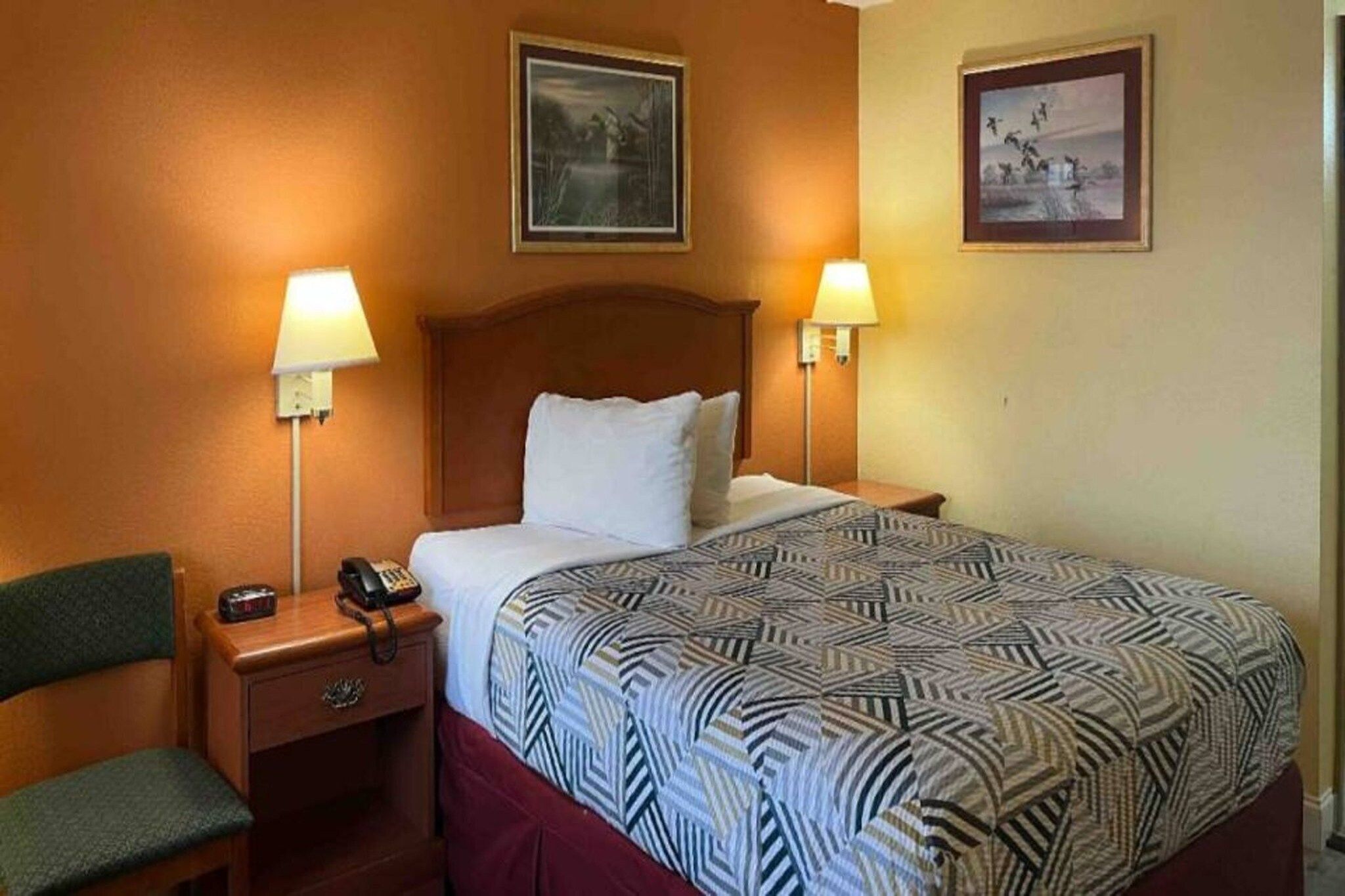 A hotel room with a bed, two bedside lamps, a telephone, and a chair.