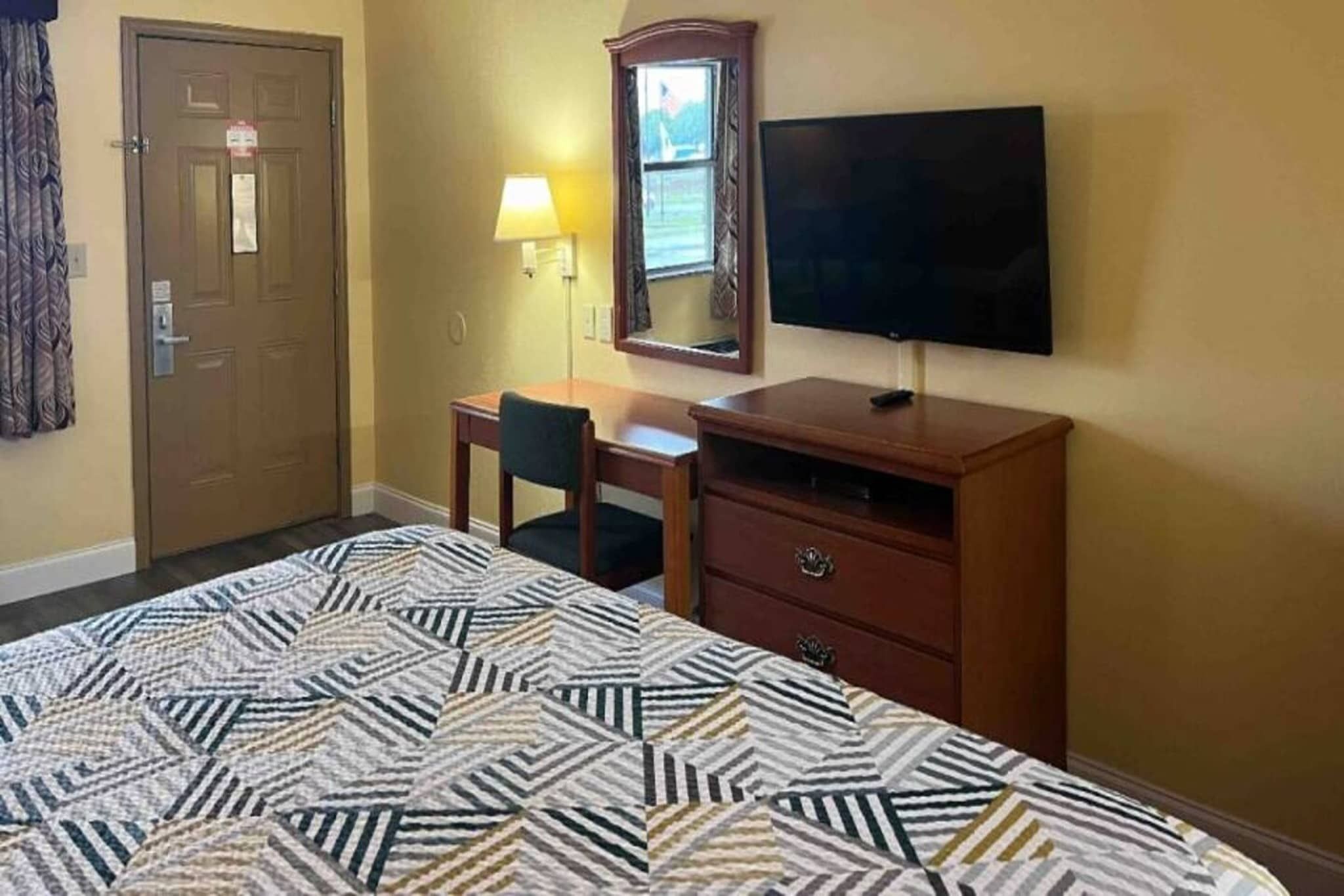 Une chambre d’hôtel équipée d’un lit, d’un bureau, d’une chaise, d’une commode, d’un téléviseur et d’une fenêtre.