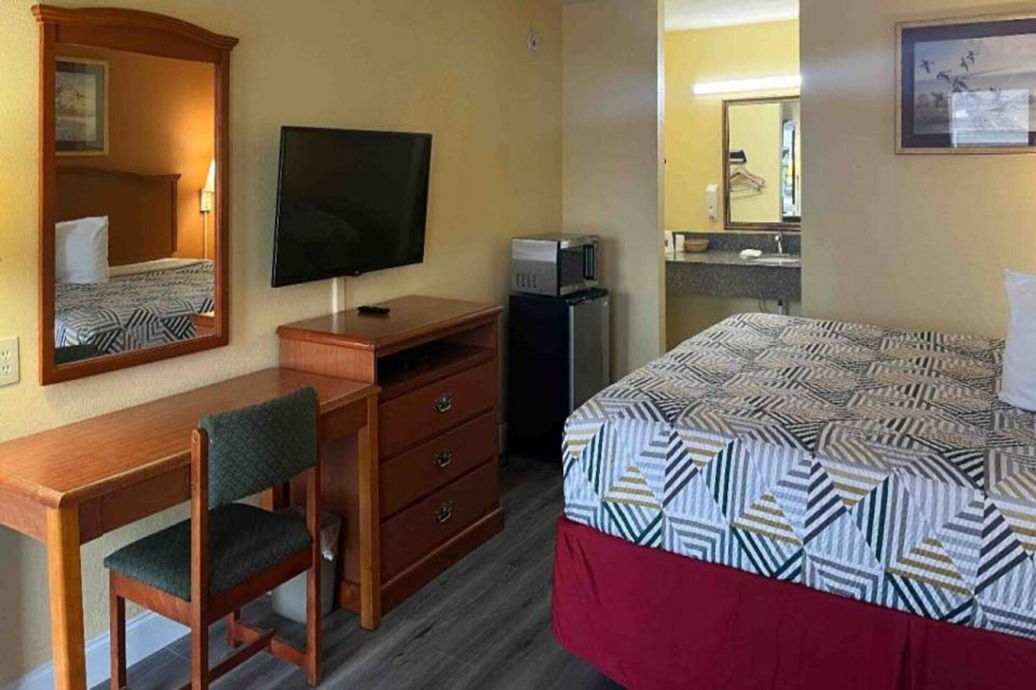 A hotel room with a bed, a desk, a chair, a television, a microwave, and a dresser.