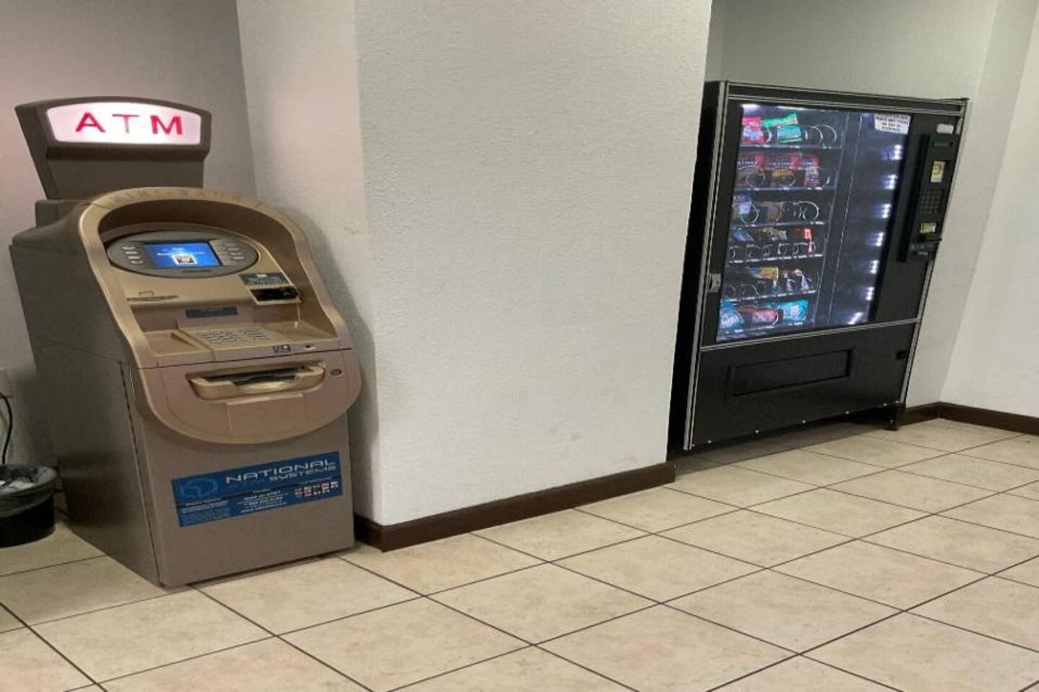 Un distributeur automatique de billets et un distributeur automatique de boissons ou de produits divers se trouvent dans un couloir.