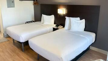 Two single beds with white linens in a room with a dark headboard and a bedside lamp.