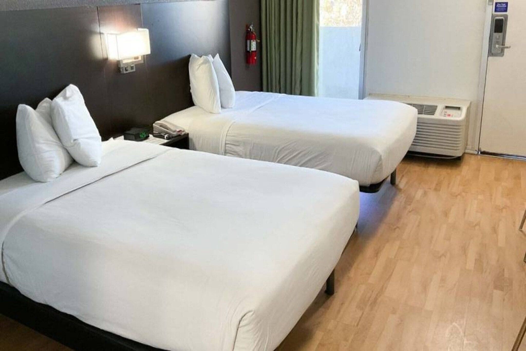Une chambre d’hôtel avec deux lits, une table de chevet, une lampe, un extincteur et un appareil de climatisation.