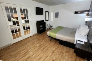Une chambre à coucher comprenant un lit, une commode, une chaise, un téléviseur et une porte donnant sur une autre pièce.