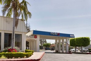A motel with a covered parking area, palm trees, and a clear sky. - 2 Queen Beds | Non-Smoking (Claremont)