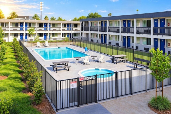A hotel with a swimming pool, outdoor seating, and a fenced area.
