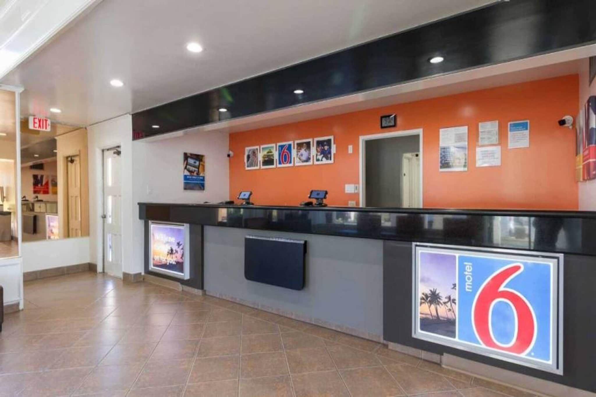 A hotel reception area with a counter, a digital screen, and a wall with numbered signs.